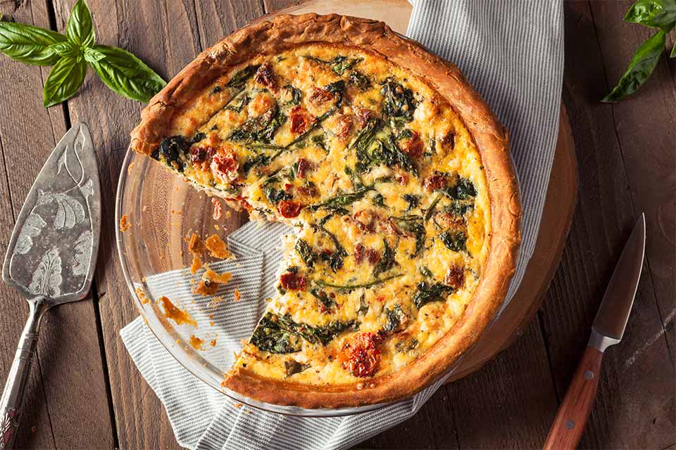 A quiche with spinach on top and a slice missing